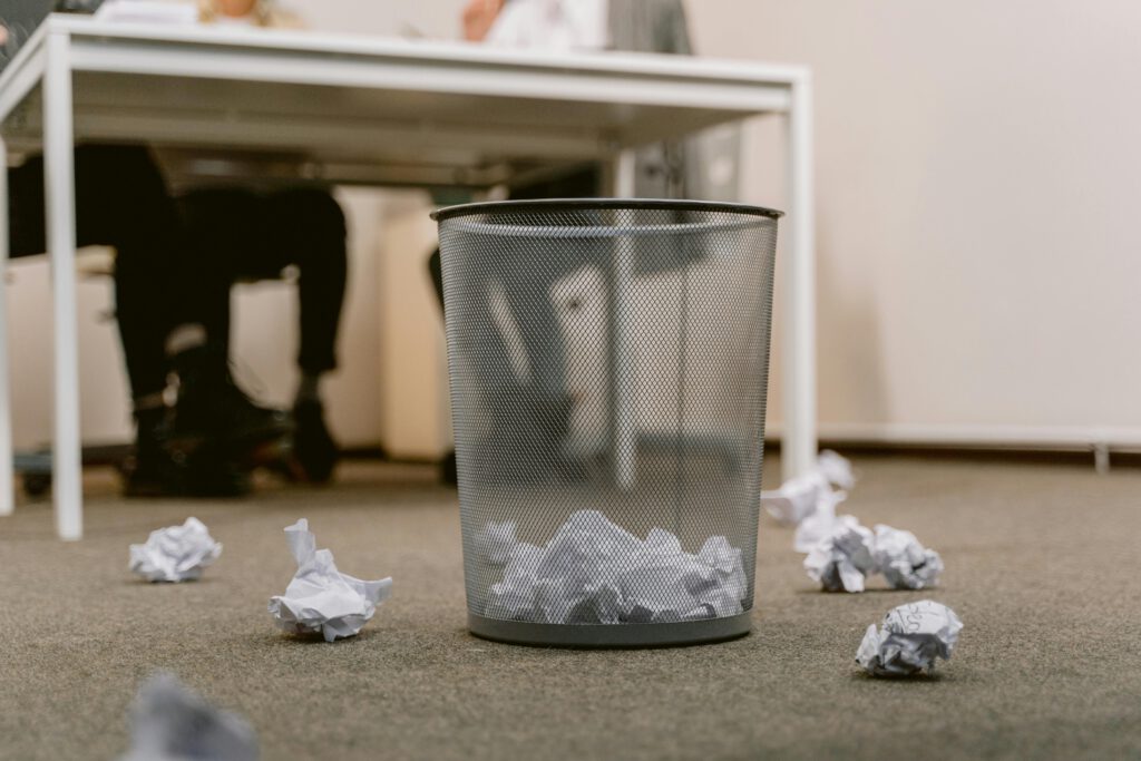 pexels photo 6913195 6913195 Office floor with a visible trash bin and crumpled papers scattered around, blurring human figures.