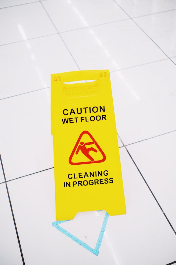 about-us-02 Bright yellow caution wet floor sign on white tiled floor indoors.